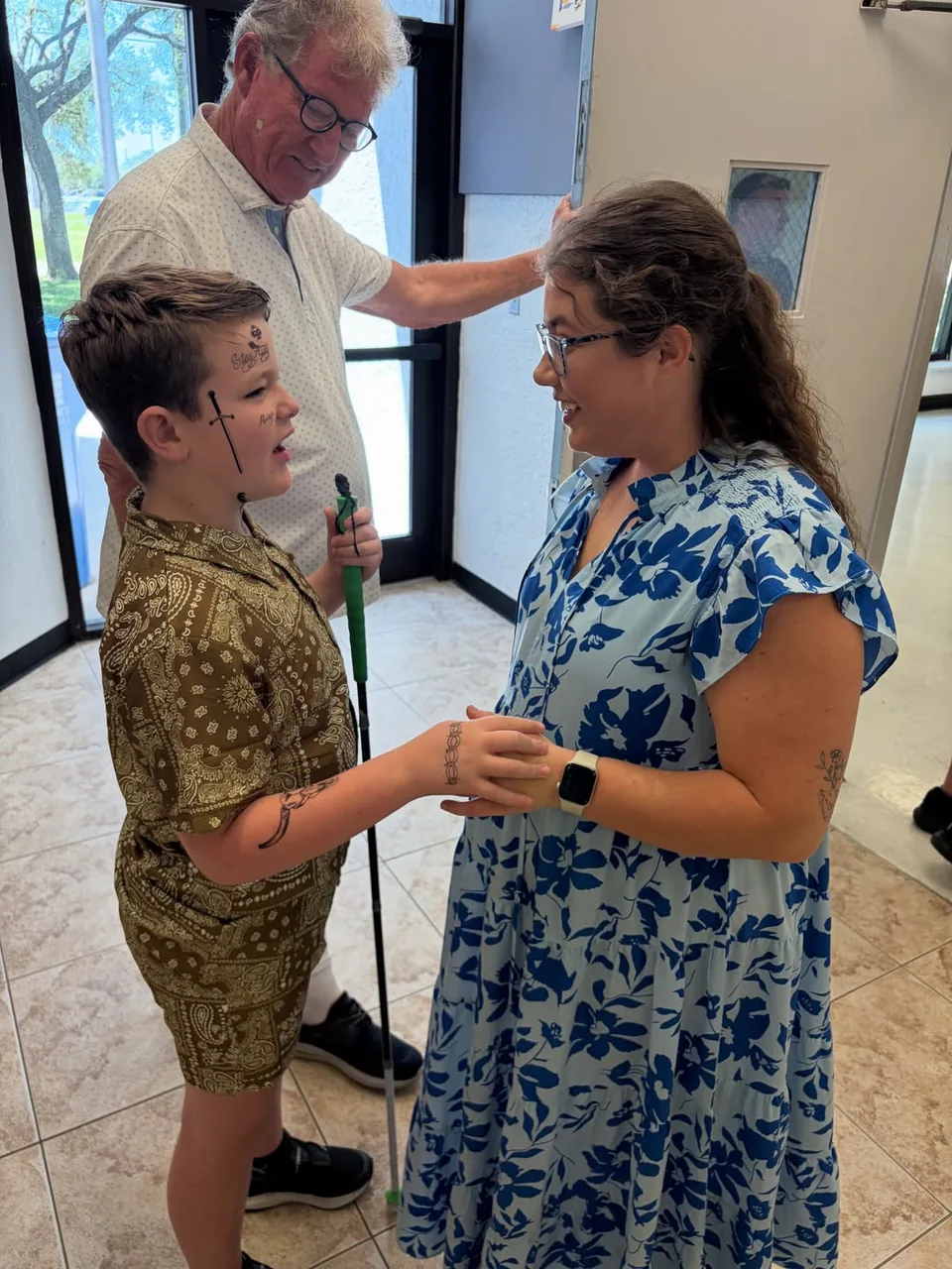 A board-certified music therapist in a floral dress gently holding hands with a young boy in a warm, connected moment.