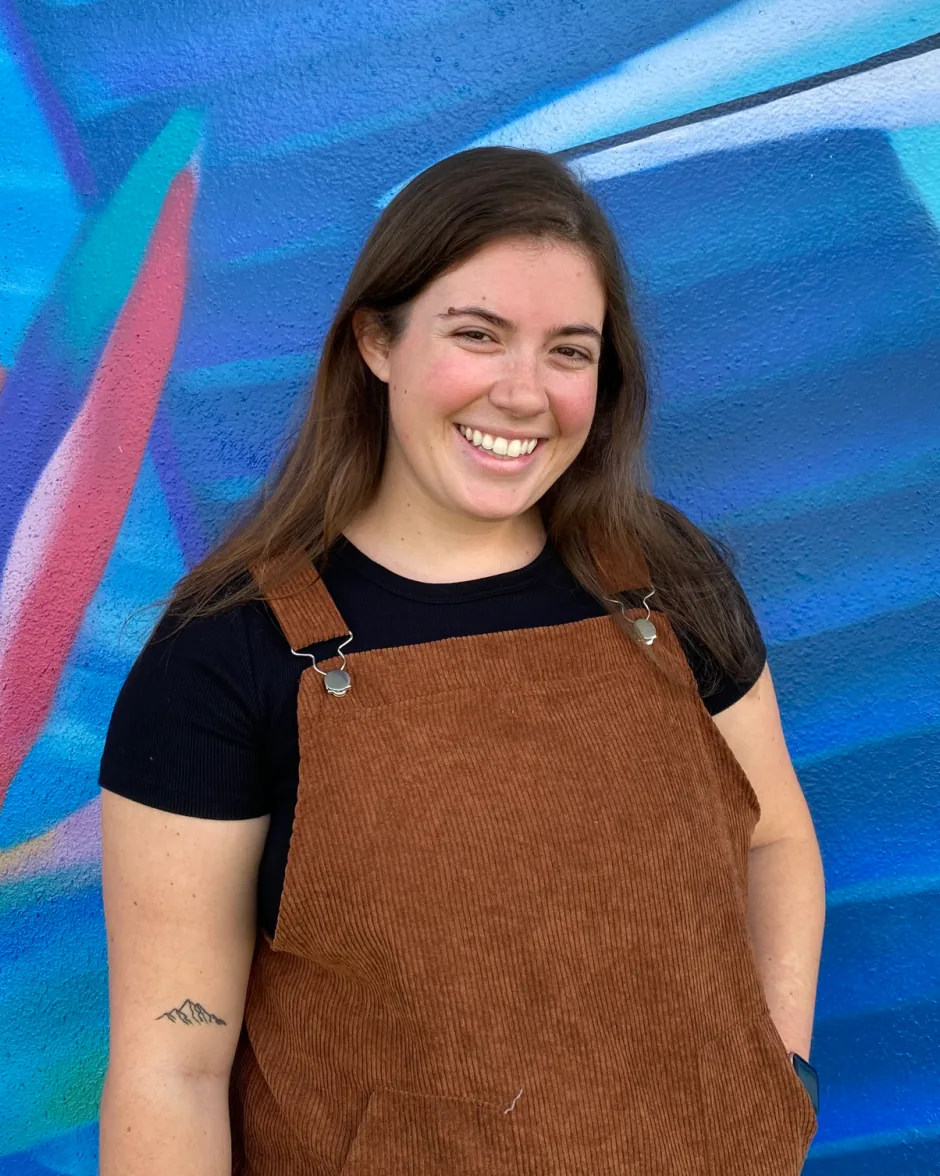 Brooklyn C. Webb, board-certified music therapist (MT-BC), smiling in front of a colorful mural