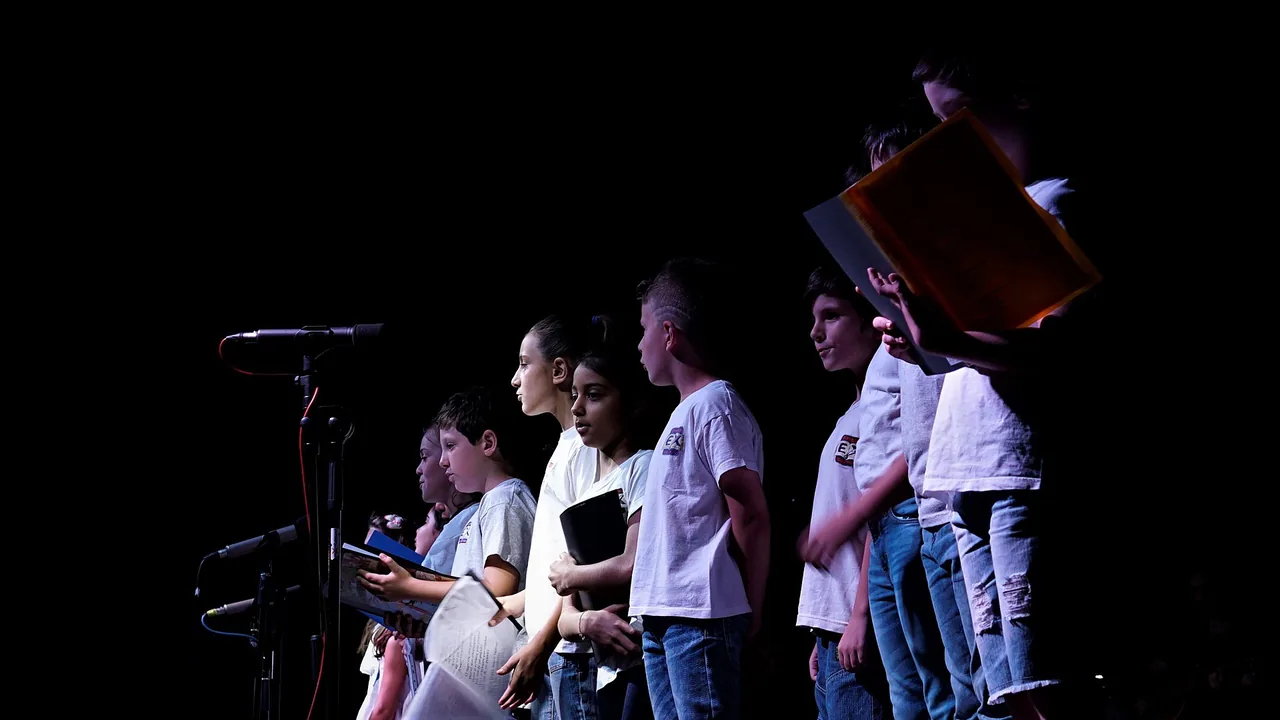 A group of children sing together into a microphone on a small stage.